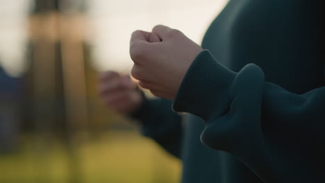 초록색 옷을 입고 손목을 회전시키는 개인의 클로즈업, 흐릿한 배경, 움직임의 감각을 만들고 손목 행동에 초점을 맞추는, 야외 설정에서 포착