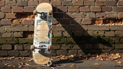 a unique perspective on an abandoned skateboard leaning against a brick wall surrounded by fallen leaves and casting a long shadow in the morning light