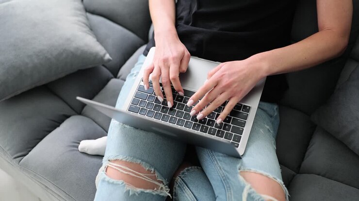 Person typing on a laptop while sitting on a couch
