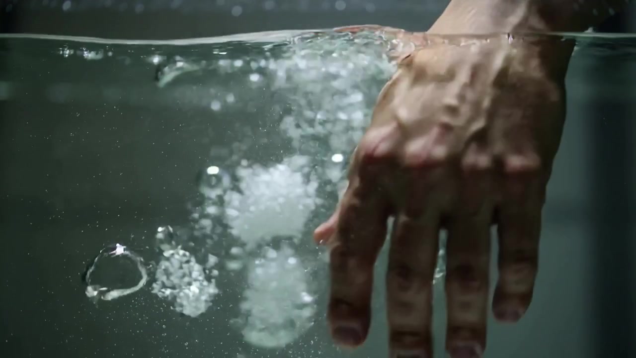 Mano di uomo adulto che rilascia aria e forma una colonna di bolle in ascesa in una vasca d'acqua trasparente.