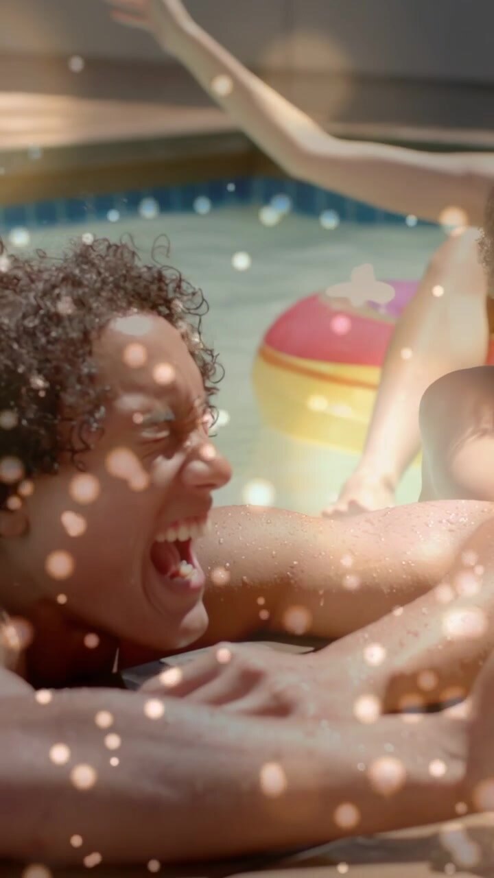 Vertical video: Sunlight sparking man leaning and laughing while woman on float gesturing, chatting