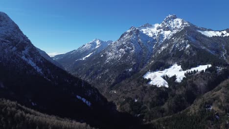 Aerial-view-over-pine-forest-in-between-of-huge-mountain-landscape-in-late-winter-in-Austria