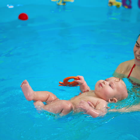 smiling woman supporting a baby lying on the water surface in the swimming pool. female coach having a lesson of swimming with a kid.