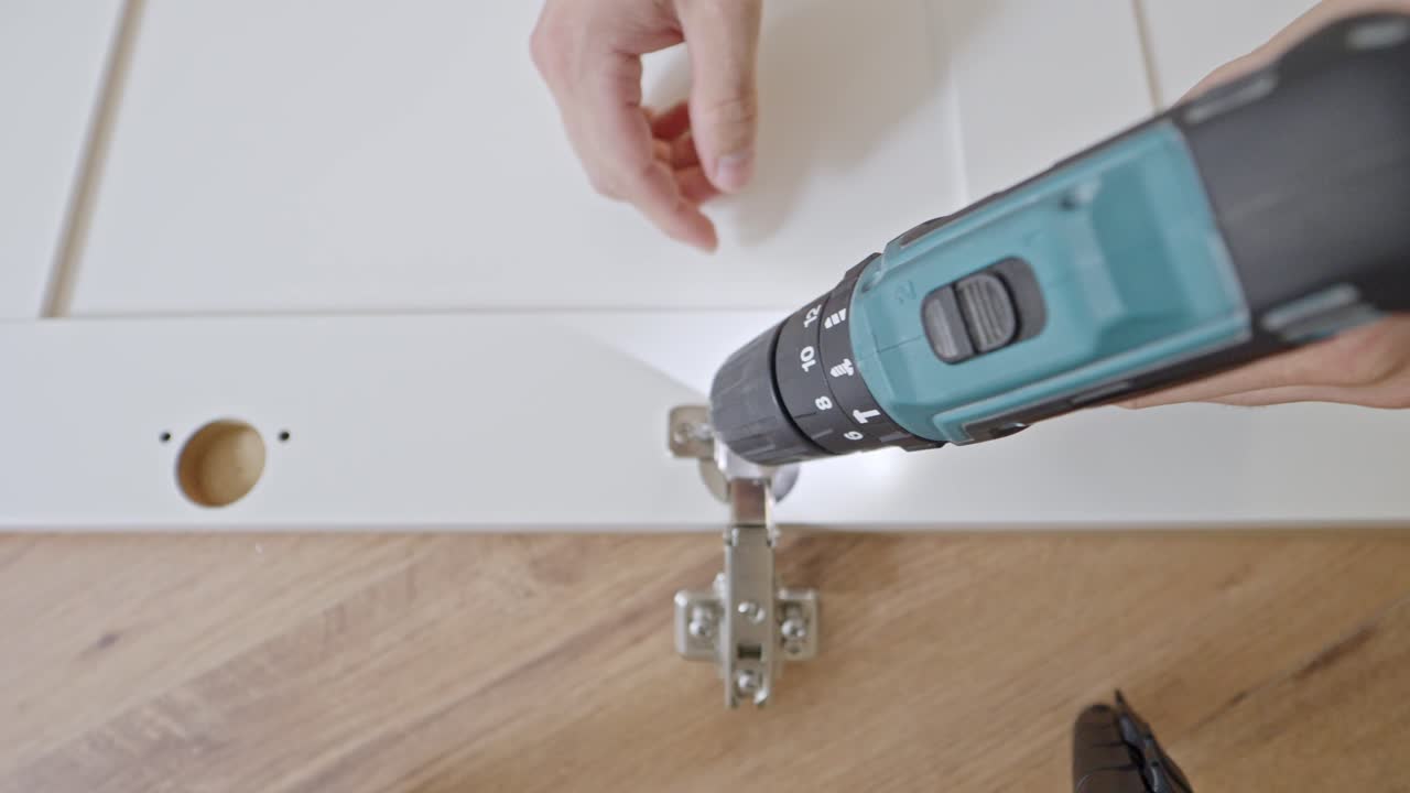 위에서 아래로 볼 수 있는 전력 드릴로 옷장 문 힌지를 스크루링하는 것