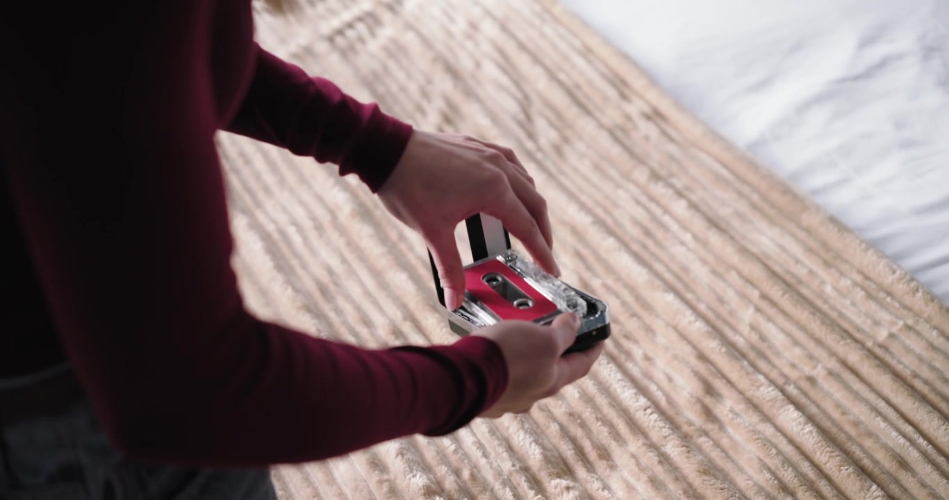 Adult woman maroon top preparing cassette and player with earbuds on bedspread to listen