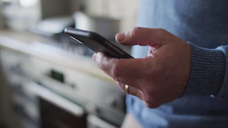 Primer-Plano-De-Las-Manos-De-Un-Hombre-Caucásico-Usando-Un-Teléfono-Inteligente-En-La-Cocina-De-Casa