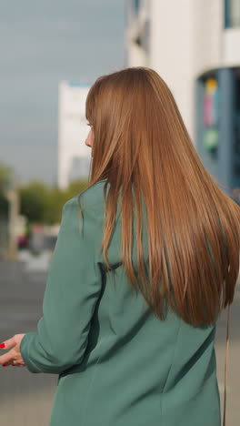 busy woman discusses household chores with relatives using mobile phone. worried female rushes home against building facade at sunlight backside view