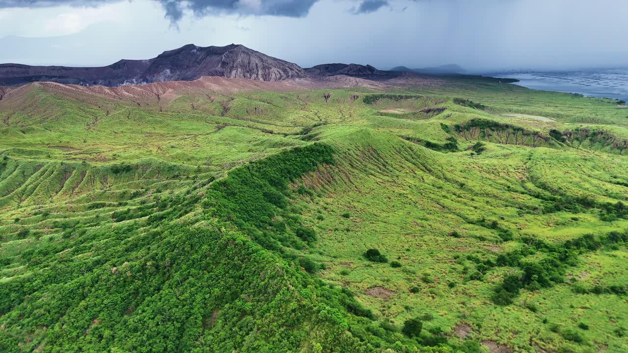 Aerial shot towards Taal Volcano in the Philippines on a cloudy summer day, with thick clouds overhead and distant rain, highlighting the moody, dramatic landscape over Taal Lake.