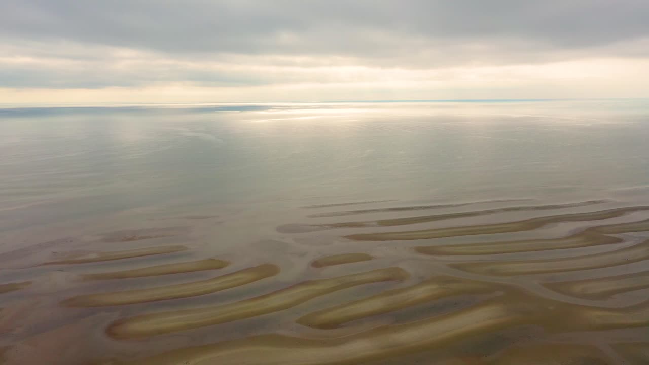 Maine beach at low tide reveals wave-like sandbars, shallow tidal pools glistening across the flats, and natural dunes forming along the edges of the sandy coastal landscape