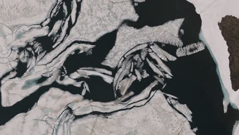 broken ice and snow block texture on dark water of bachalpsee lake switzerland, drone top down rising