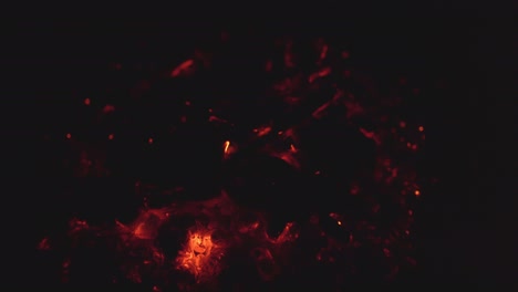 close-up shot of glowing embers burning inside a fire ring at night. the heat radiates as the coals smolder and flicker in the darkness.