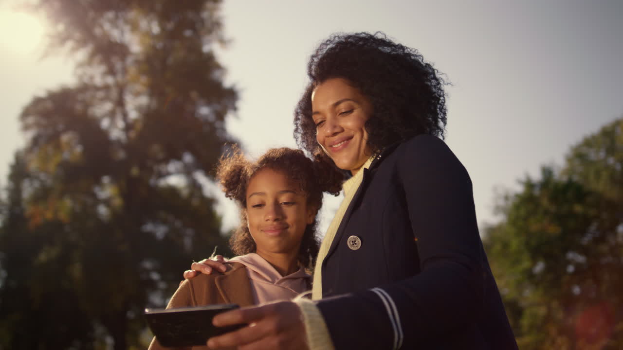 madre feliz sosteniendo un teléfono inteligente haciendo selfies con su linda hija en el parque de primavera.