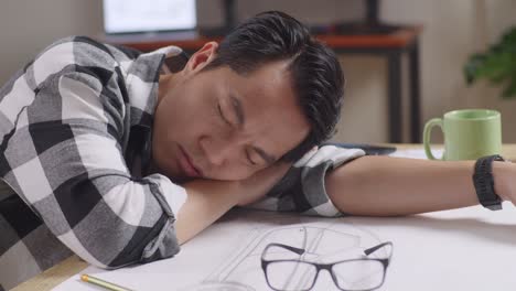 close up of asian male sleeping while working on a car design sketch on table in the studio