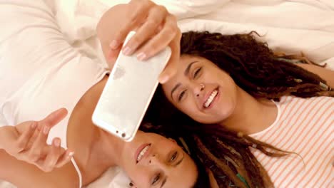 una pareja feliz de lesbianas en la cama tomando selfies.