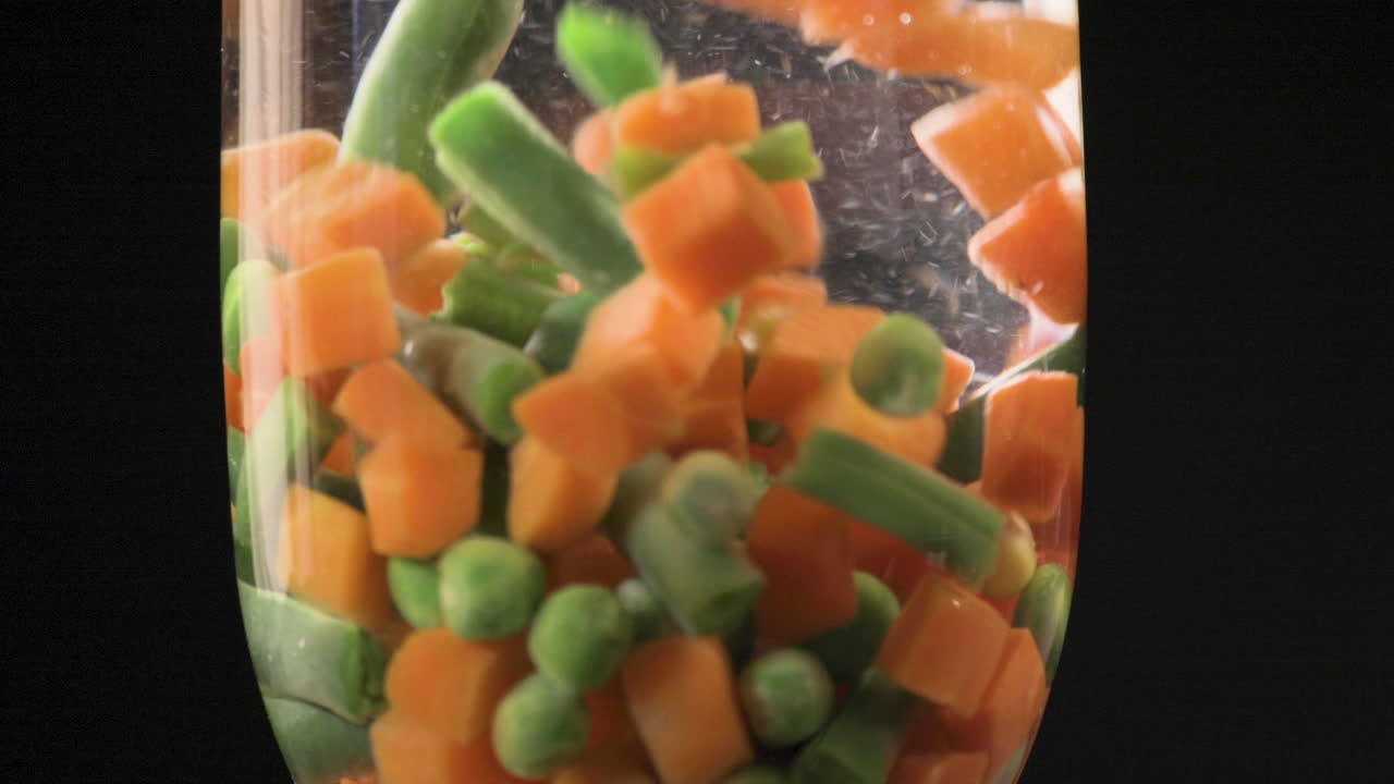 Misto di verdure fresche lasciate cadere nell'acqua con una combinazione colorata su sfondo nero e ripreso in 4K
