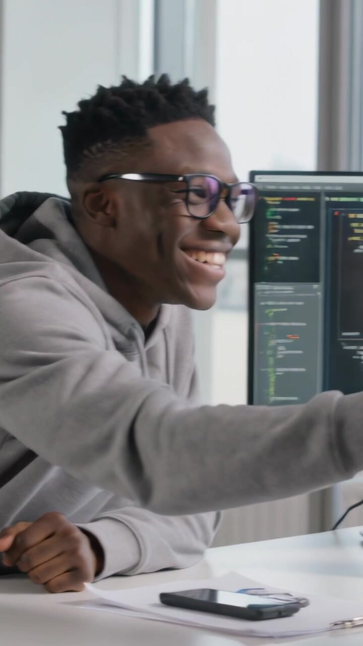 Vertical video: Turning hoodie man pointing at code monitor in office with peer nearby, copy space