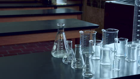 paneo a través de un banco de laboratorio negro con una variedad de cristalería química en el laboratorio de química de la escuela secundaria