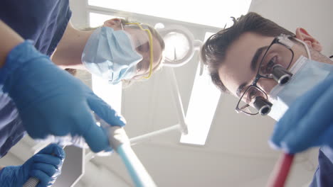 upward pov of dentist with glasses and female assistant treating dental disease