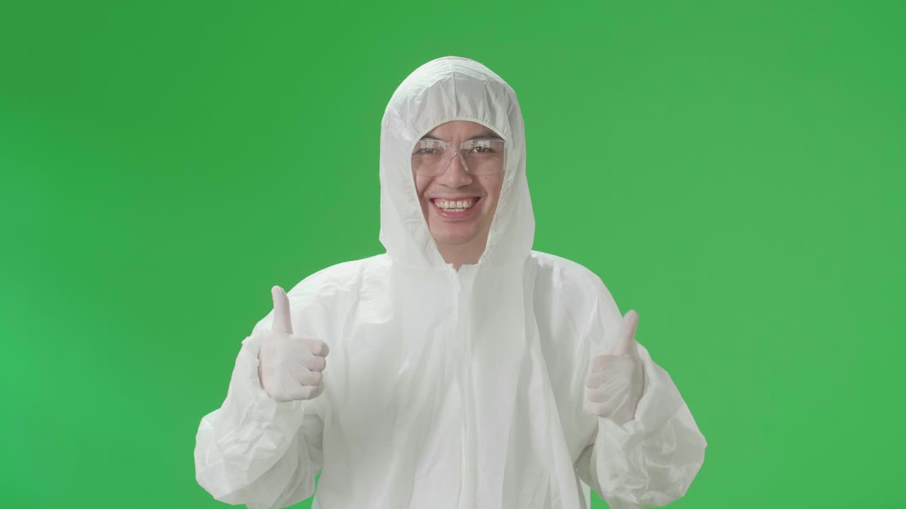 Asian Male Wearing Personal Protective Equipment Uniform Ppe And Showing Thumbs Up In Green Screen Studio
