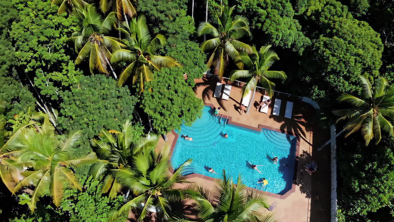 Aerial view of a swimming pool surrounded by lush tropical trees with people enjoying a swim