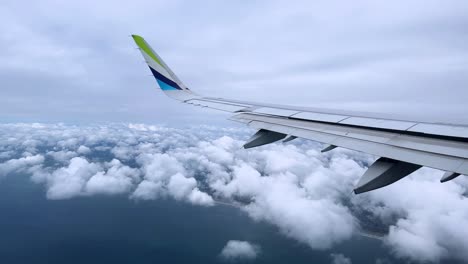 view of a plane wing soaring above clouds during daytime from a passenger window seat