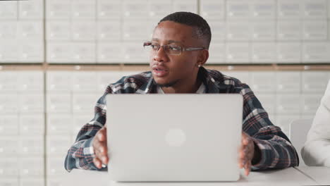 african american student touches laptop thinking. black guy in glasses uses computer for education against card index cases. technologies of 21st century