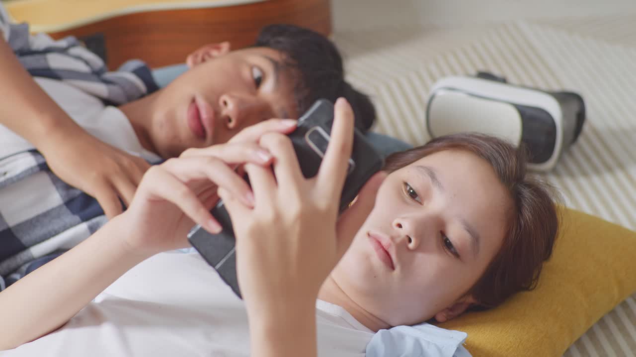 집에서 바닥에 카에 누워있는 아시아 십대 커플의 가까운 사진. 화가 난 소녀가 스마트폰을 사용하고 남자친구를 무시하고, 화가 난 남자친구가 그녀에게 관심을 기울이려고 시도한 후 그릴 친구를 혼자 떠난다.