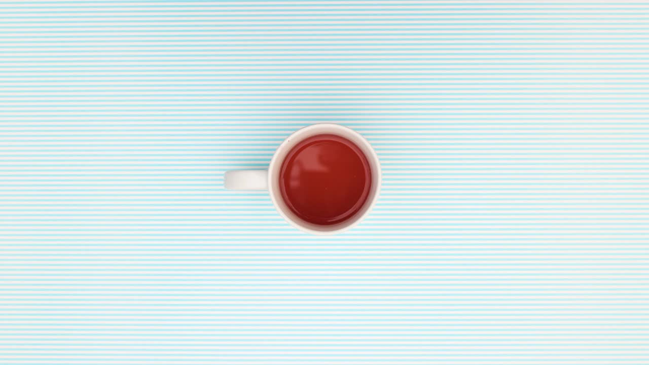 여성의 손가락은 파란색 배경에 서클로 차의 세라 컵을 움직입니다.