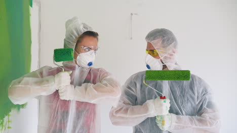 pareja en trajes de protección posa con rodillos de pintura en la habitación