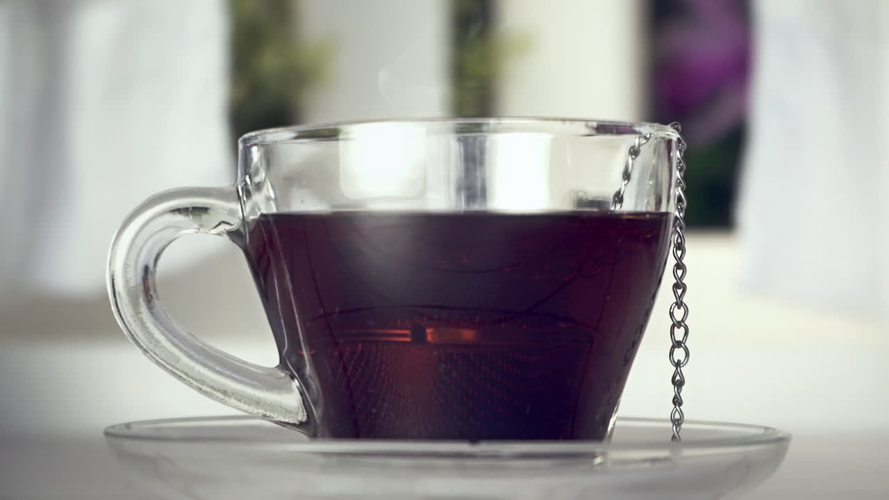 Mano che rimuove l'infusore da tè da una tazza di vetro fumante