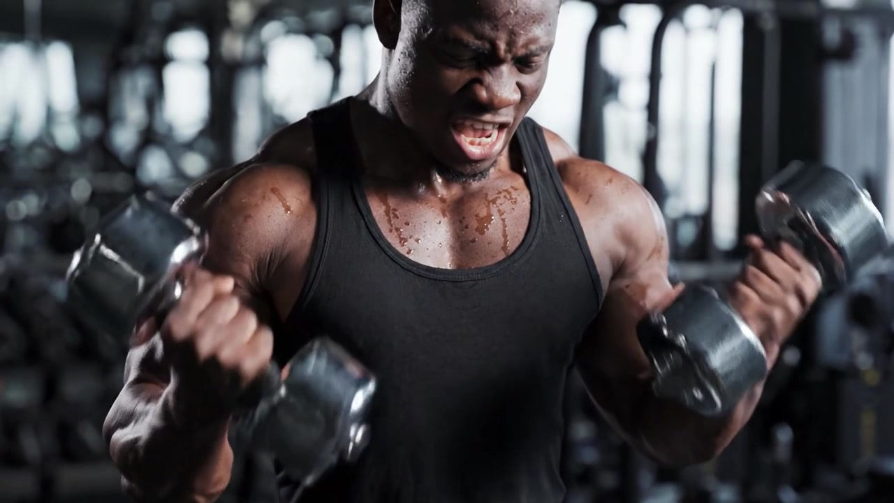 A focused individual demonstrating strength and determination while lifting weights at a gym, showcasing impressive muscle definition and intense concentration during a workout session.