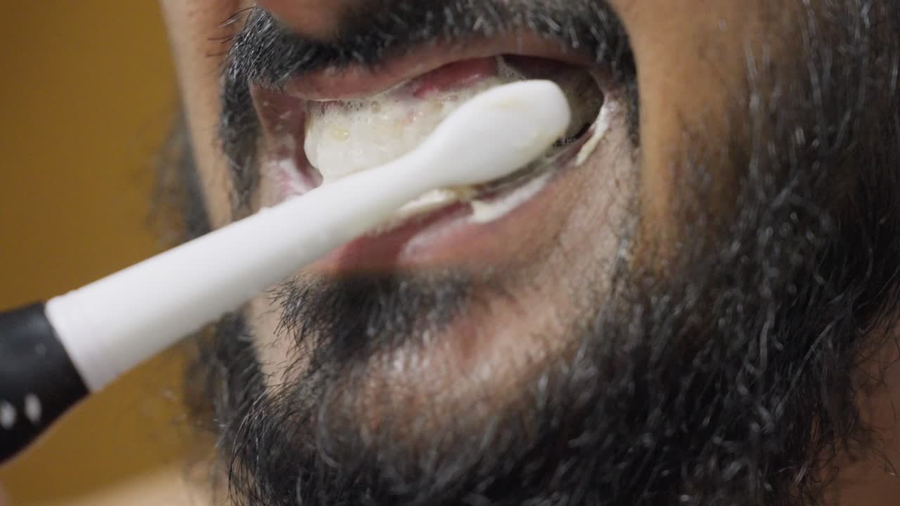A slow-motion, close-up footage of a South Asian man brushing his teeth, with a blurred background. Dental care and hygiene concept