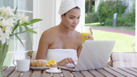 Young-woman-using-a-laptop-while-having-breakfast