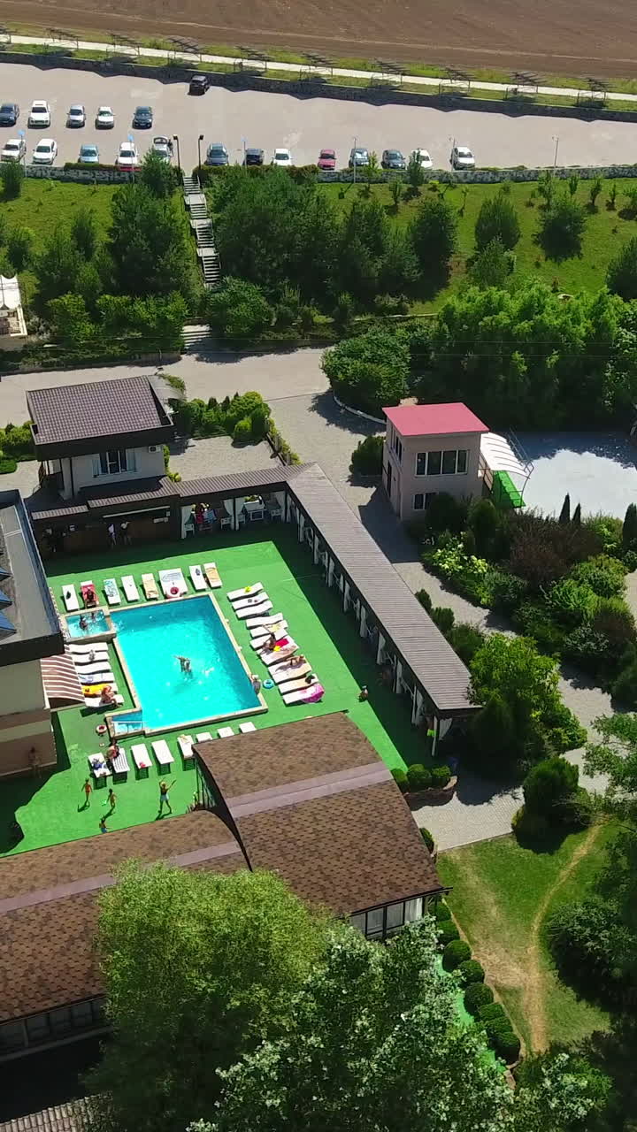Green, clean and well-structured territory of spa-resort outside the city. Luxury outdoor swimming pool and relaxing zone around it. Birdseye view. Vertical video