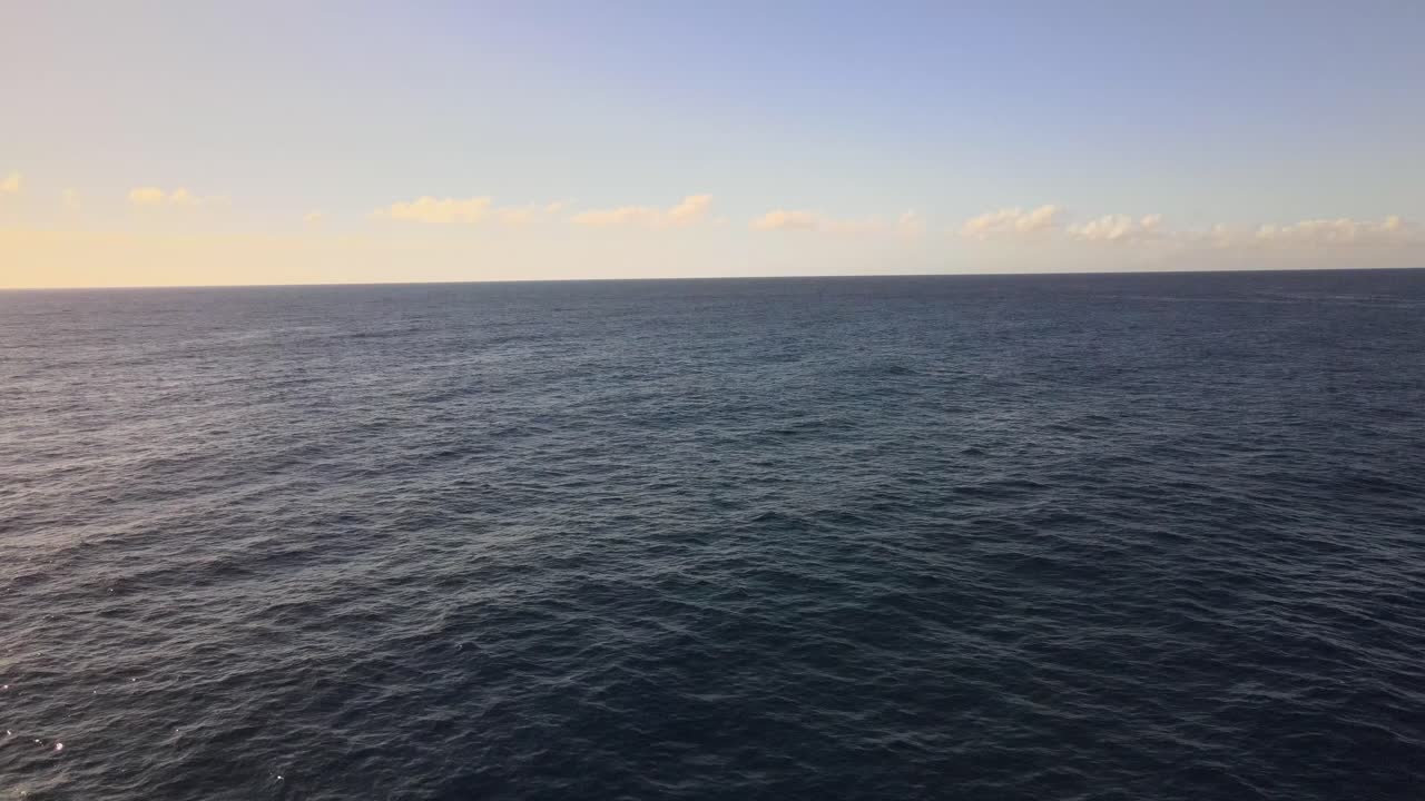Una serena prospettiva da drone che domina il mare aperto con il tramonto appena fuori campo, proiettando una bellissima sfumatura dal chiaro allo scuro, mentre onde leggere si formano in lontananza.