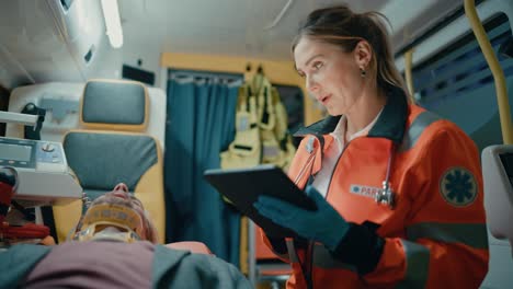 female ems professional paramedic using tablet computer to fill a questionnaire for the injured patient on the way to hospital. emergency care assistant comforting the patient in an ambulance.