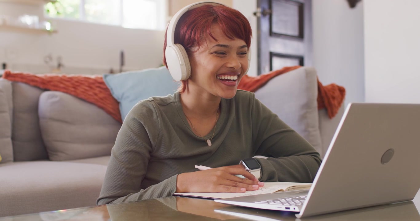 African American woman joining online session at home, waving and laughing at laptop, taking notes