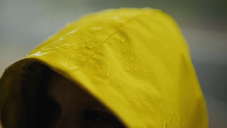 Close-up-a-teenage-girl-in-a-yellow-jacket-and-hood-stands-in-the-rain-drops-of-water-fall-on-the-hood-and-flow-down-from-it-during-heavy-rain