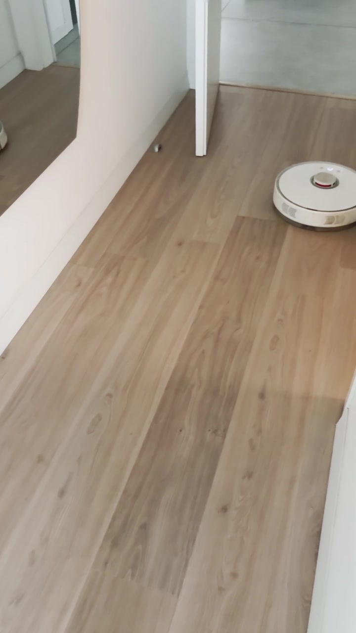 Cleaning robot driving around in apartment ugc pov phone style shot on parquet wooden floor inside house. Technology in home passing by sweeping floor automatically. Funny busy round robot working