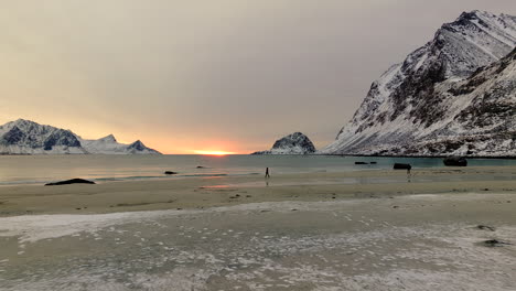 Two-people-on-arctic-Haukland-beach-in-snowy-landscape,-Lofoten