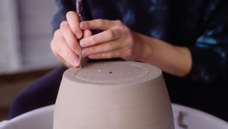 Potter-scores-clay-pot-on-pottery-wheel