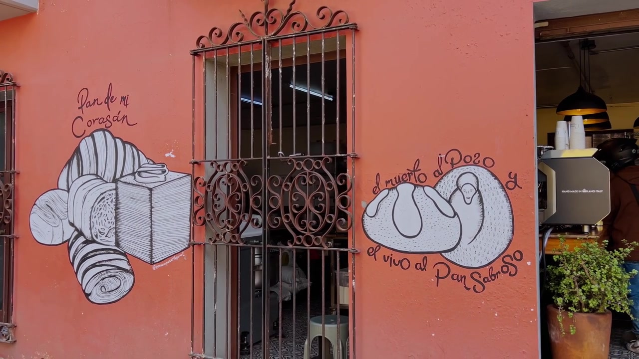 Murale stradale messicano con illustrazioni disegnate a mano di pane tradizionale e scritte in spagnolo su una parete esterna colorata, accanto a una vetrina con inferriate a Huatulco, Messico.