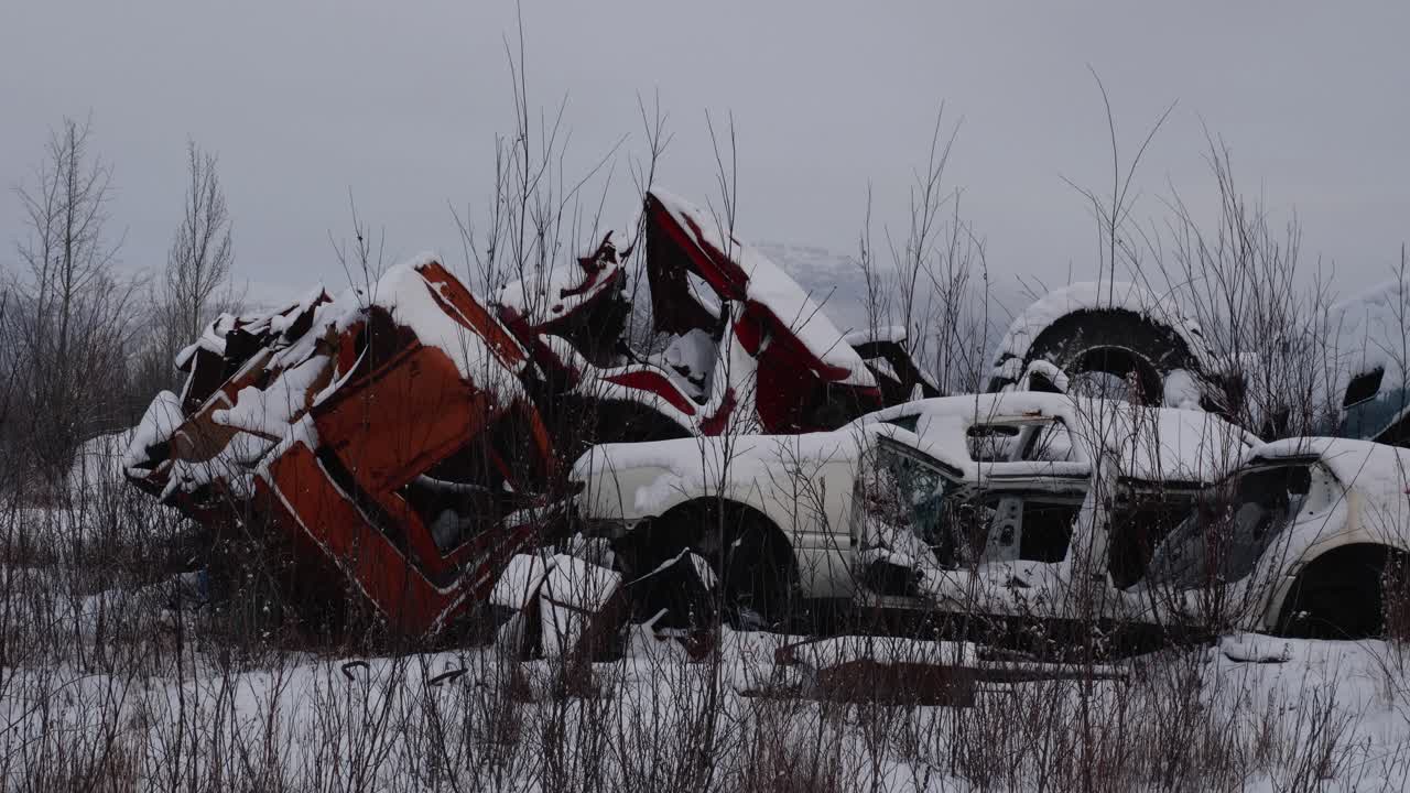 Snow-covered vehicles rest in a desolate junkyard. A bleak winter landscape of abandoned and decaying automobiles