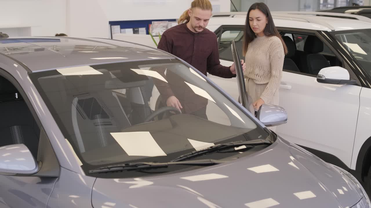 una hermosa pareja de jóvenes en la sala de exposición de automóviles eligiendo un coche nuevo para comprar.