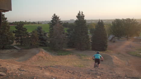 man on mountain bike flies by the camera and launches over a wood ramp on top of a hill