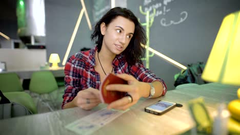 young girl with short black hair, dressed in a shirt on a hand watch, sitting at the bar at the airport coffee shop, waiting for his departure, considering his passport, and communicates with someone