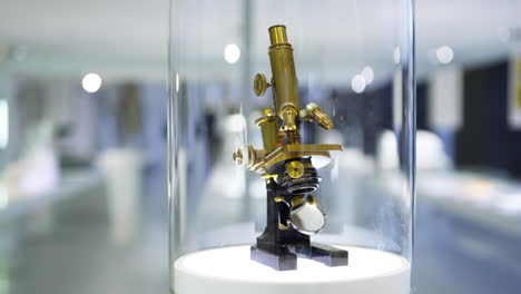 pan down to an ancient microscope model made from brass, being displayed in an optics museum showcase