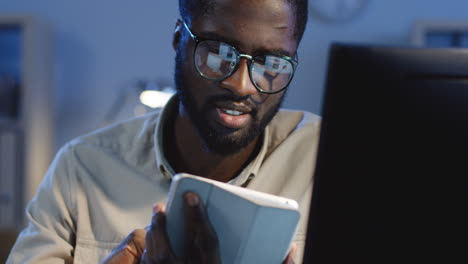 close up view of young cheerful man in glasses using his tablet in the office at night