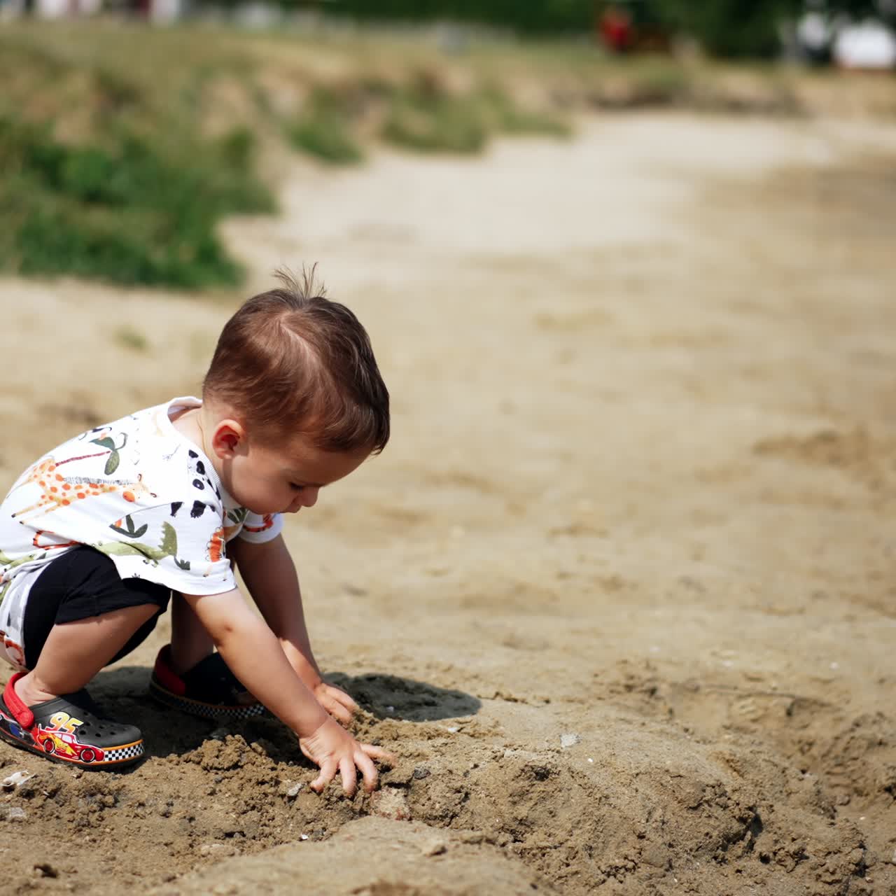 Un adorabile bambino caucasico è concentrato sul suo gioco con la sabbia. Il bambino è seduto sulla riva del fiume e prende la sabbia tra le mani. Vista dall'alto