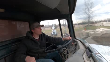 Man-inside-1972-dump-truck-driving-into-construction-site